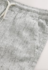 Shorts en lin gris clair avec tissu texturé, taille élastique et cordon de serrage. Dotés de poches latérales pour plus de praticité.