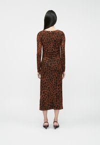 Pikad varrukad, keha järgiv kleit pruunis, mustade südame mustritega. Poolte sääre pikkus, kogutud selja detail, kantud suletud varvastega kontsadega.