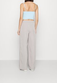 Světle modrý zkrácený top se smockovanou texturou, spárovaný s kalhotami s vysokým pasem a širokými nohavicemi v světle šedé barvě, které mají jemné vertikální pruhy.