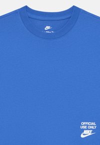 Mėlyna Nike marškinėliai su baltais užrašu "OFFICIAL USE ONLY" ir Nike logotipu atspaustas apatiniame dešiniajame kampe.