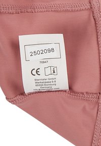 Rosa Stoffetikett mit Pflegehinweisen und CE-Kennzeichnung; Naht entlang der Kanten; enthält Produktcode und Kontaktdaten des Unternehmens.