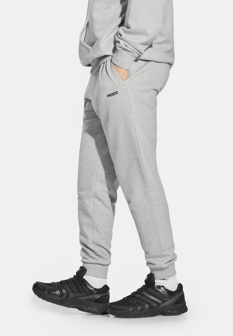 Szare dresy wykonane z mieszanki bawełny, z bocznymi kieszeniami i elastycznym paskiem. Czarne trampki o teksturowanym wykończeniu i białe skarpetki.