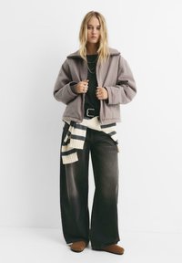 Lys grå jakke med bred krave, sort skjorte under, oversized mørke jeans, kremfarvet og marineblå stribet tørklæde og brune sko.