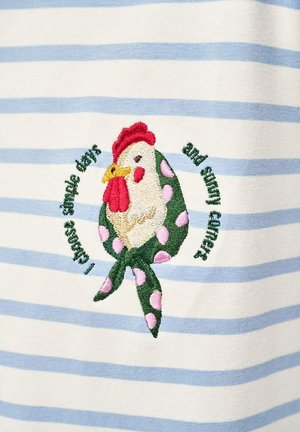 Wyhaftowany kurczak w zielonym szaliku w różowe kropki na białej i jasnoniebieskiej pasiasttej tkaninie, otoczony tekstem ułożonym w okrąg.