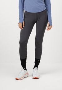 Atletische leggings van donkergrijs materiaal, met een gladde textuur, met een aansluitend ontwerp en bijpassende zwarte enkelaccenten.