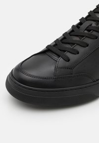 Sneaker in pelle nera con suola in gomma testurizzata, lacci neri coordinati e dettagli di cucitura sottili. Design della punta arrotondata per un aspetto moderno.