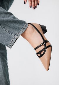 Zapato beige de punta con detalles en negro, con un tacón ancho y una textura suave. Combinado con un denim azul claro.
