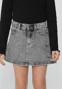 Jupe en denim noire et grise avec taille haute, fermeture à boutons sur le devant, poches et embellissements étoilés usés.