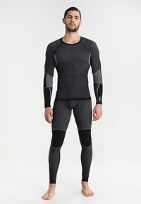 Maglietta a maniche lunghe nera e leggings, con tessuto testurizzato, cuciture bianche a contrasto e toppe sulle ginocchia per un supporto maggiore.