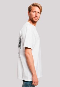 White cotton t-shirt with short sleeves, featuring a black graphic of trees on the back. Round neckline, relaxed fit, and soft texture.