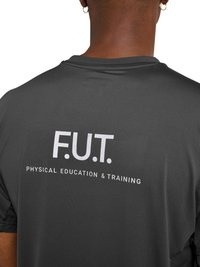 Back view of a person wearing a dark gray shirt with "F.U.T. Physical Education & Training" printed in white on the upper back.