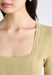 Knit top in light green with a square neckline, featuring textured ribbing and vertical lines. Smooth fabric with a fitted design.