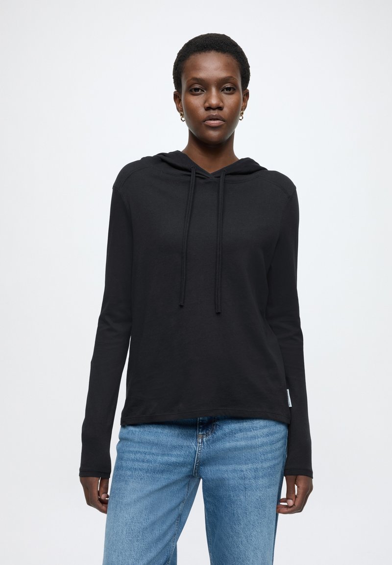 Μαύρη μπλούζα με κουκούλα από μαλακό ύφασμα με κορδόνι, μακριά μανίκια και άνετη εφαρμογή, σε συνδυασμό με μπλε τζιν παντελόνι.