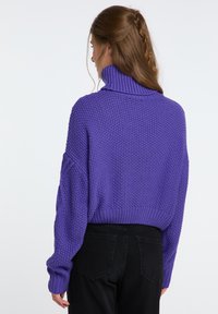 Fialový pletený sveter s dizajnom roláku, textúrovaným vzorom a rebrovanými manžetami. Nosený s čiernymi nohavicami s vysokým pásom.