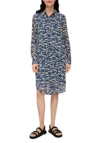 Robe chemise à motifs bleus et crème avec un col, des manches longues et une coupe décontractée. Portée avec des sandales noires à lanières. Tissu léger.