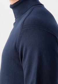 Navyblauer Rollkragenpullover aus weichem Material, mit geripptem Kragen und Schulternähten sowie einer glatten Textur. Seitenansicht dargestellt.