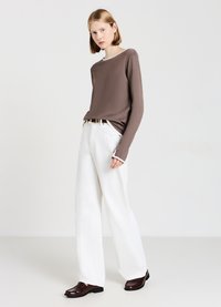 Maglietta marrone a maniche lunghe con scollatura rotonda, abbinata a pantaloni bianchi larghi e mocassini marroni scuri. Tessuto morbido e vestibilità rilassata.