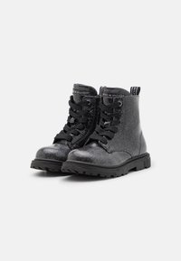 Botines brillantes negros con cordones en la parte frontal, suelas de goma y puntera reforzada. Cuenta con una lengüeta y detalles de costura en contraste.