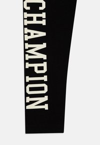 Leggings neri in cotone con la scritta bianca "CHAMPION" stampata in verticale lungo il lato. Caratterizzati da una consistenza liscia e una cintura elastica.