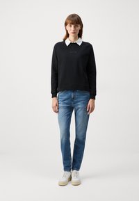 Black sweatshirt with a round neckline, white collared shirt underneath, light blue jeans, and white sneakers with beige soles.