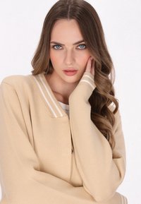 Beige gebreide cardigan met witte gestreepte kraag en manchetten, met een losse pasvorm en naadloos ontwerp. Glad textuur en minimale details.