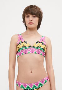 Le haut de bikini coloré présente un motif géométrique avec des accents rose, vert, jaune et noir. Il a des bretelles larges et un décolleté en V.