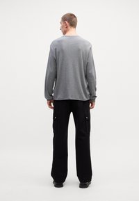 Γκρι μακριά μπλούζα με διακριτή υφή, σε συνδυασμό με μαύρα cargo παντελόνια με πλαϊνές τσέπες και χαλαρή γραμμή.