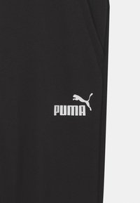 Czarne spodnie sportowe o miękkiej fakturze, z białym logo Puma na lewej udzie i prostym wzornictwie bez dodatkowych wzorów.