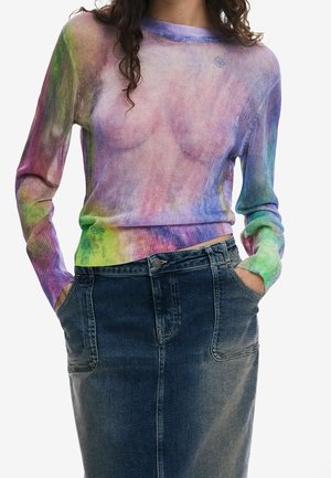 Femme portant un haut transparent à manches longues tie-dye aux couleurs pastel et une jupe en denim foncé taille haute avec des poches avant.