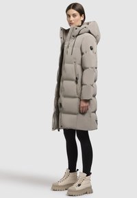 Gaisa pūšļi beļģu krāsā ar kapuci, ar rāvējslēdzēju, lielu quilted dizainu un sānu kabatām. Apvienots ar beļģu krāsas masīviem zābakiem.