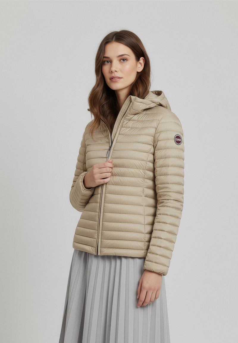 Beige gewatteerd jack met capuchon, voorzien van een doorgestikt ontwerp, ritssluiting en een logobadge op de linkermouw. Gemaakt van een gladde, lichtgewicht stof.