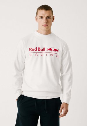 Sweat à capuche blanc avec un grand logo rouge "Red Bull Racing" sur la poitrine et deux graphismes de taureaux rouges. Manches longues avec des poignets côtelés.