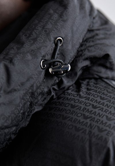 Crna jakna s anorakom s sjajnim metalnim detaljima, koja sadrži zatvaranje na vezicu i teksturiranu tkaninu s uzorkom "Emporio Armani".