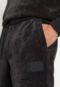 I jogger in corduroy neri presentano un tessuto testurizzato con una vestibilità ampia, tasche laterali e un patch in pelle con il logo sulla coscia sinistra.