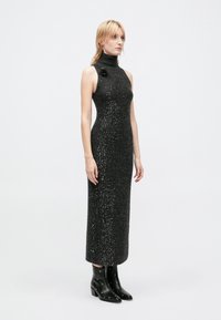 Black, sleeveless, high-neck dress with a fitted silhouette, featuring a textured, sparkling fabric and a decorative flower accent.