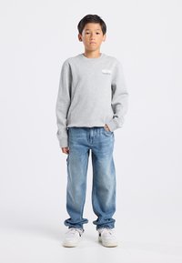 Felpa grigia con collo rotondo, vestibilità ampia, abbinata a jeans baggy di un blu chiaro e sneakers bianche. Outfit casual dal design semplice.