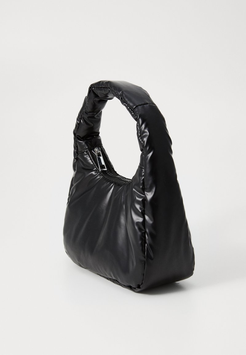 Sac à main noir rembourré avec une poignée arrondie et une fermeture éclair. Il présente une texture lisse et brillante et a une forme triangulaire.