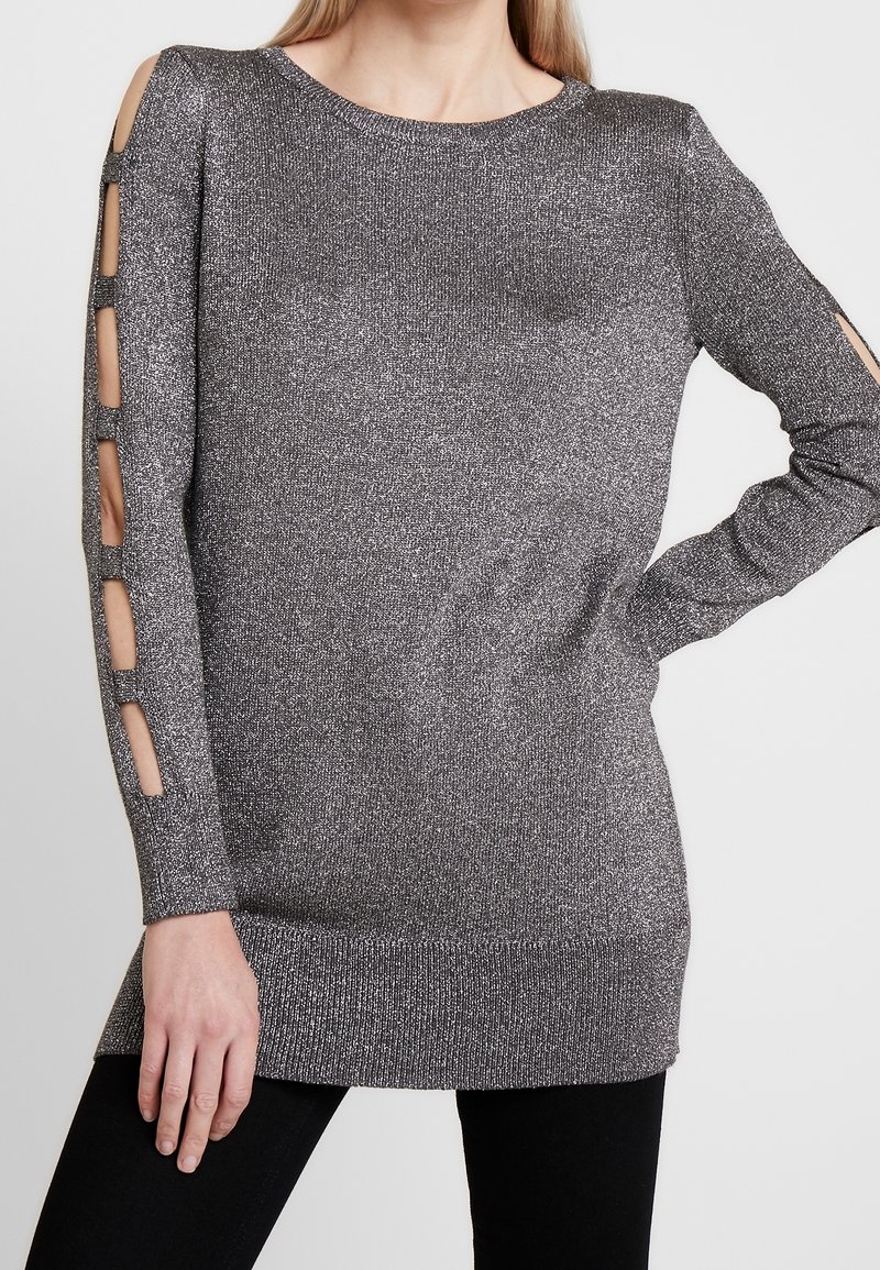 Glittrande silver långärmad tröja med axelöppningar, texturerat stickat tyg och ribbad fåll. Matchad med svarta underdelar.