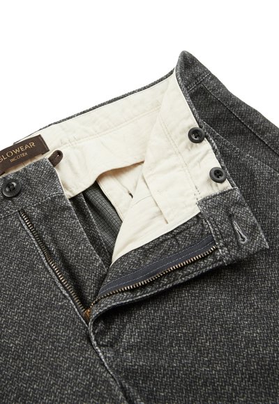 Szare spodnie w wzór w jodełkę z zapięciem na zamek błyskawiczny, dwoma czarnymi guzikami oraz białą podszewką widoczną w okolicy pasa i kieszeni.