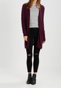 Lång lila cardigan över en svart och vit randig skjorta, tillsammans med svarta ripped skinny jeans och svarta ankelskor.