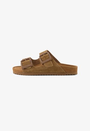 Sandale mule en daim marron avec deux brides réglables et boucles en plastique, semelle plate avec dessous rainuré pour une meilleure adhérence.