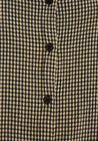 Camisa de cuadros en tejido beige y negro con una superficie texturada, que cuenta con botones en la parte frontal y un diseño de cuello clásico.
