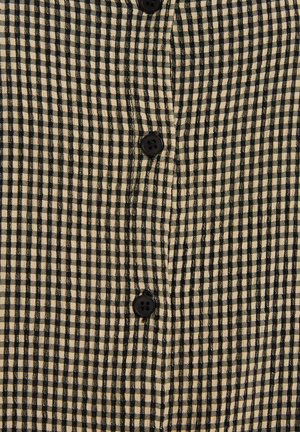 Camisa de cuadros en tejido beige y negro con una superficie texturada, que cuenta con botones en la parte frontal y un diseño de cuello clásico.