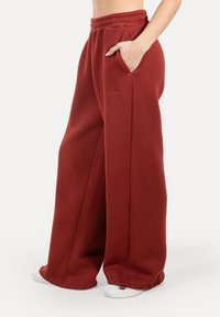 Široké tepláky v tmavě červené barvě, se stretchovým pasem, bočními kapsami a vyšitým logem. Měkký, strukturovaný materiál.