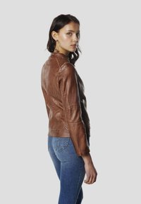 Hnedá kožená bunda s priliehavým strihom, textúrovaným povrchom a rebrovanými doplnkami na ramenách. Kombinovaná s modrými džínsami, zobrazená zo strany.