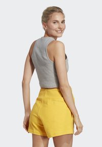 Top corto grigio abbinato a pantaloni corti gialli a vita alta. I pantaloni corti presentano tasche e un tessuto strutturato.