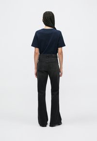 Fekete, bővülő szárú farmernadrág és tengerészkék póló, mindkettő minimalista dizájnnal; a farmerek zsebekkel és közép magas derékkal rendelkeznek.