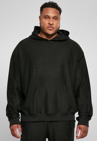 Sort ribbet hoodie med en stor frontlomme, snoretræk i hætten og løs pasform, lavet af blødt materiale; har lange ærmer og en struktureret overflade.