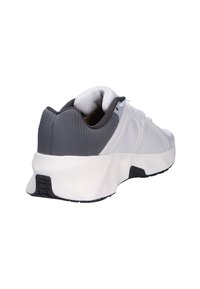 Zapatilla deportiva blanca y gris con un talón gris texturizado, parte superior de malla y una suela blanca acolchada. Presenta cordones y pequeños detalles en negro.