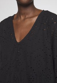 Robe en coton noir ornée de découpes brodées délicates, avec un décolleté en V et des boutons sur le devant, le tout avec une surface légèrement texturée.